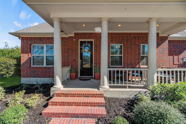 entrance to property featuring brick siding, covered porch, and roof with shingles