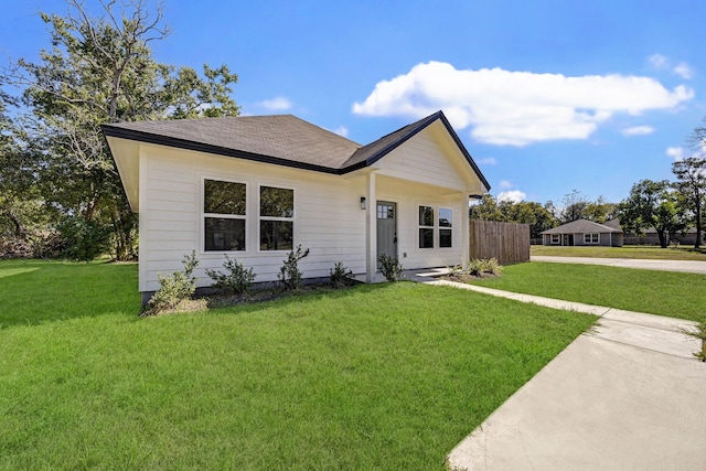 view of front of property featuring a front yard, fence, and a shingled roof