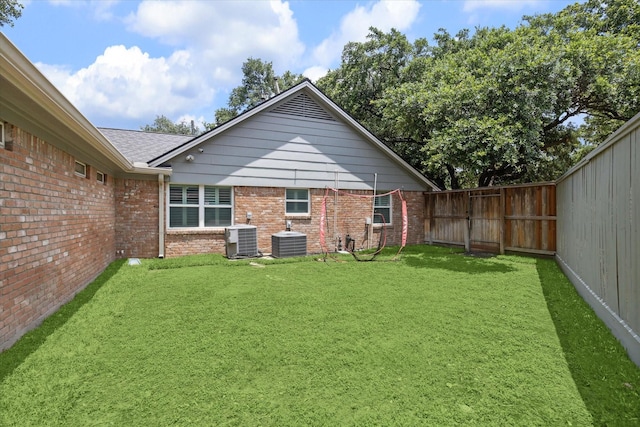 rear view of house featuring central air condition unit, a fenced backyard, brick siding, and a lawn