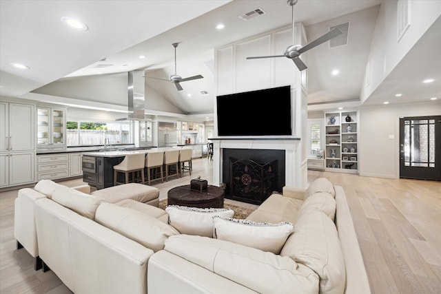 living area featuring a ceiling fan, visible vents, high vaulted ceiling, light wood-style flooring, and a fireplace