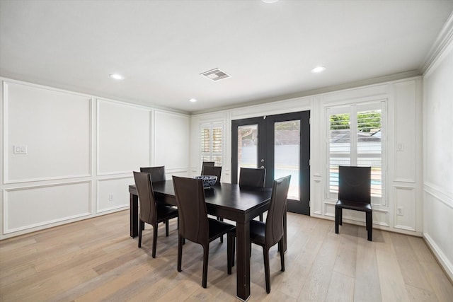 dining space featuring light wood finished floors, a decorative wall, french doors, and visible vents