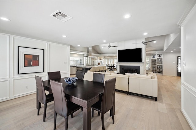 dining space featuring a fireplace, a decorative wall, light wood-style floors, and visible vents