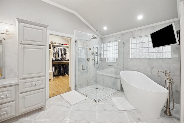 bathroom with a spacious closet, a shower stall, lofted ceiling, ornamental molding, and a freestanding tub