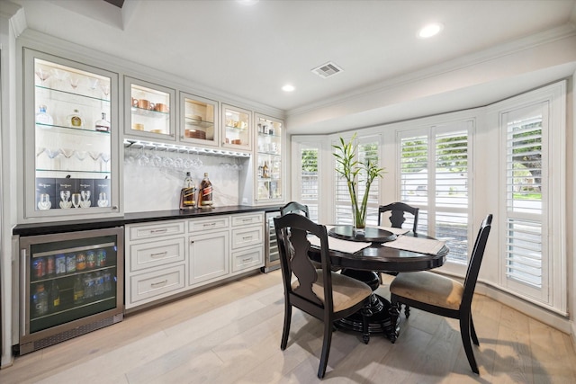 interior space featuring light wood-type flooring, visible vents, wine cooler, crown molding, and a dry bar