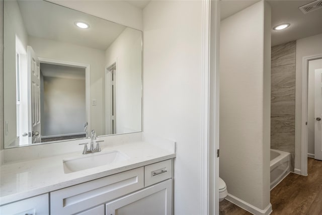 full bath with visible vents, toilet, a bathing tub, wood finished floors, and vanity