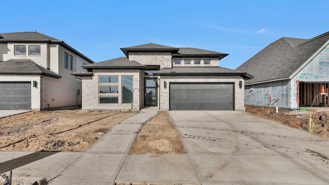 prairie-style house featuring brick siding, concrete driveway, a garage, and a shingled roof