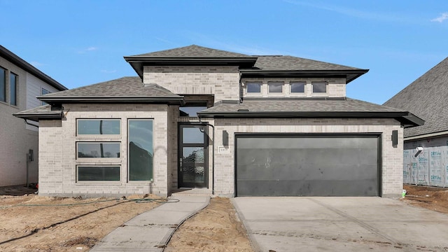 prairie-style house with brick siding, concrete driveway, and a shingled roof