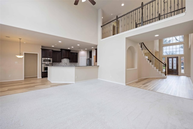 unfurnished living room featuring baseboards, light carpet, a towering ceiling, and stairs