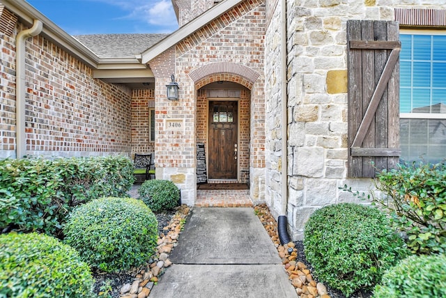 doorway to property with brick siding, stone siding, and roof with shingles