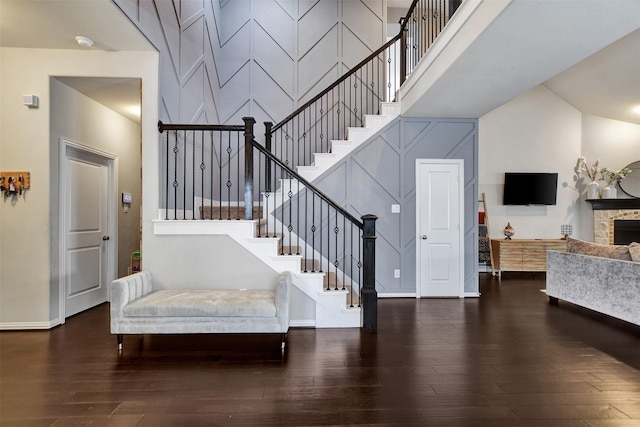 interior space featuring a stone fireplace, wood finished floors, baseboards, and a towering ceiling