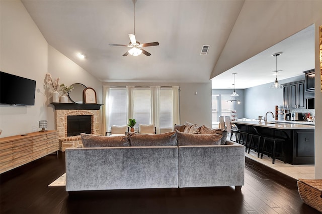 living room with visible vents, a fireplace with raised hearth, dark wood-style flooring, ceiling fan, and vaulted ceiling