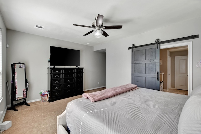 carpeted bedroom featuring visible vents, baseboards, a barn door, and a ceiling fan