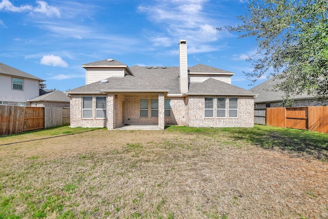 rear view of house with brick siding, a chimney, a fenced backyard, a yard, and a patio area