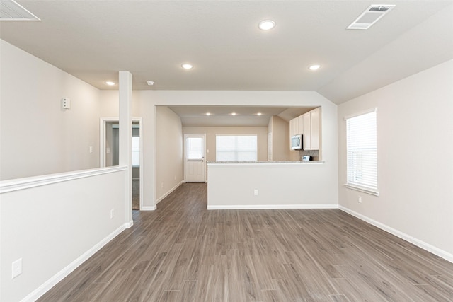 unfurnished living room featuring light wood-type flooring, visible vents, baseboards, and lofted ceiling