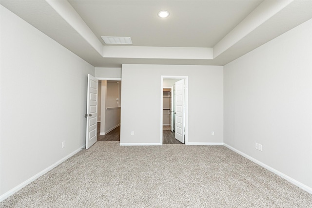 unfurnished bedroom with a tray ceiling, baseboards, visible vents, and a spacious closet