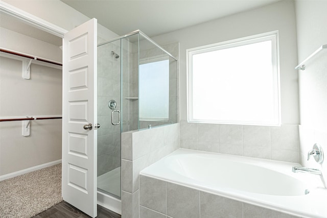 bathroom with a spacious closet, a stall shower, a bath, and baseboards