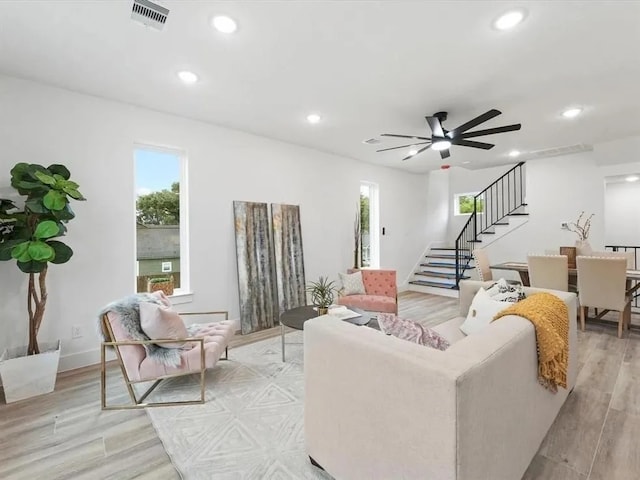 living room with a wealth of natural light, visible vents, light wood-style flooring, recessed lighting, and stairs