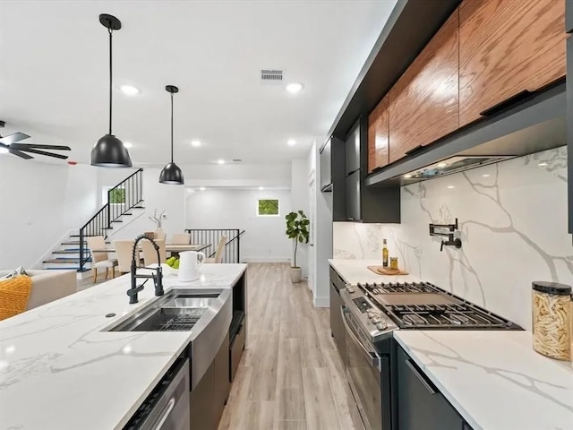 kitchen with light wood-style flooring, a sink, backsplash, dark cabinetry, and appliances with stainless steel finishes