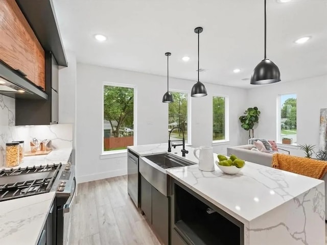 kitchen with a kitchen island with sink, a sink, light wood-style floors, appliances with stainless steel finishes, and decorative backsplash