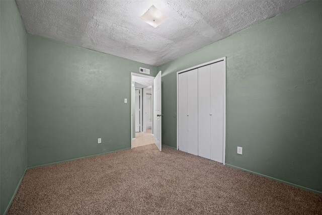 unfurnished bedroom with visible vents, a textured ceiling, a closet, carpet floors, and a textured wall