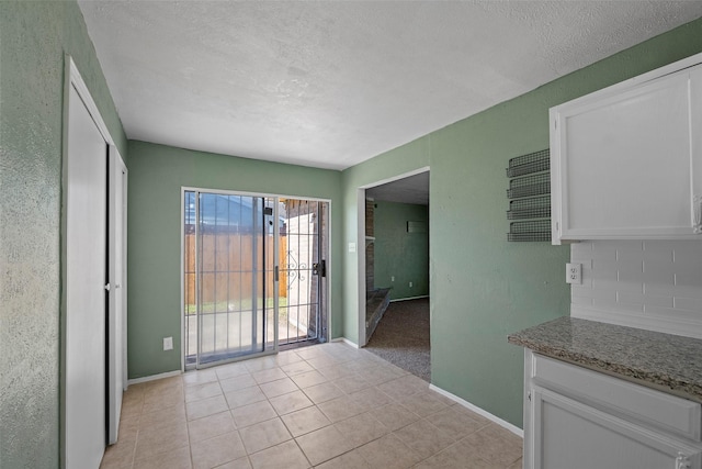 kitchen with light tile patterned flooring, white cabinets, baseboards, and backsplash