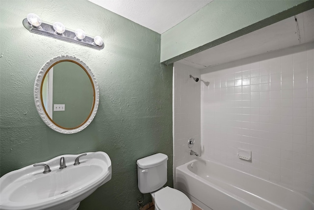 bathroom with a sink, toilet, shower / tub combination, and a textured wall