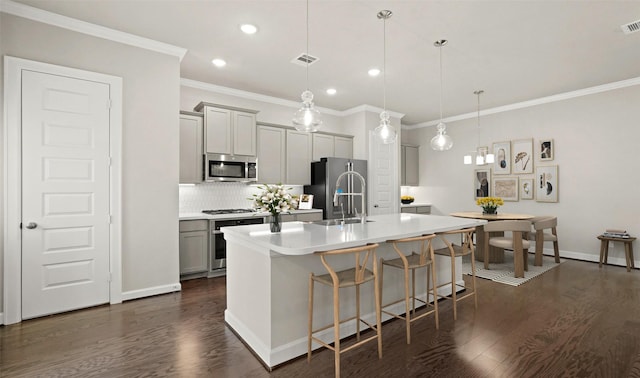 kitchen with dark wood-type flooring, appliances with stainless steel finishes, a breakfast bar, and an island with sink