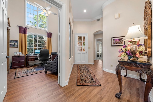 entryway featuring visible vents, arched walkways, ceiling fan, light wood-style floors, and a towering ceiling