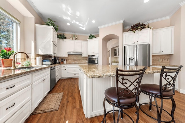 kitchen with a sink, under cabinet range hood, a kitchen island, white cabinetry, and stainless steel appliances