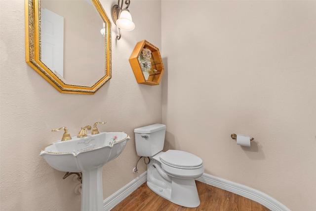 half bathroom featuring toilet, baseboards, and wood finished floors