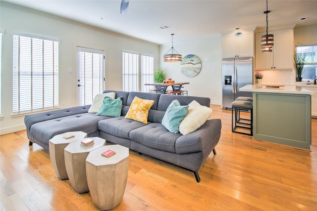 living area with light wood-style floors, plenty of natural light, visible vents, and ornamental molding