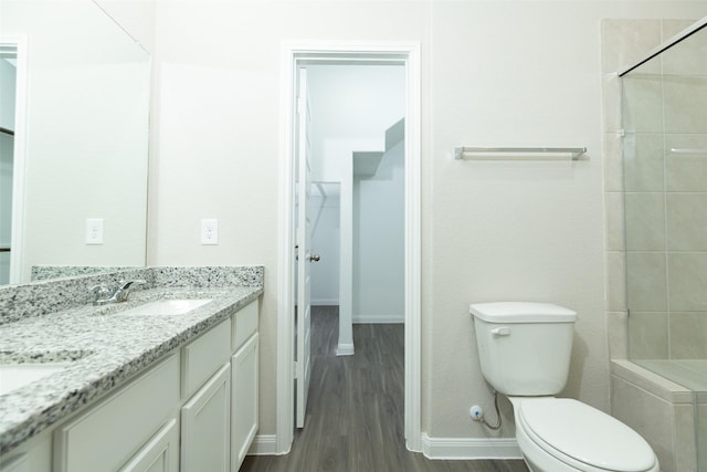 13774 Sunshine Peak Dr, Willis, TX 77318 - bathroom featuring wood finished floors, double vanity, a tile shower, a sink, and toilet