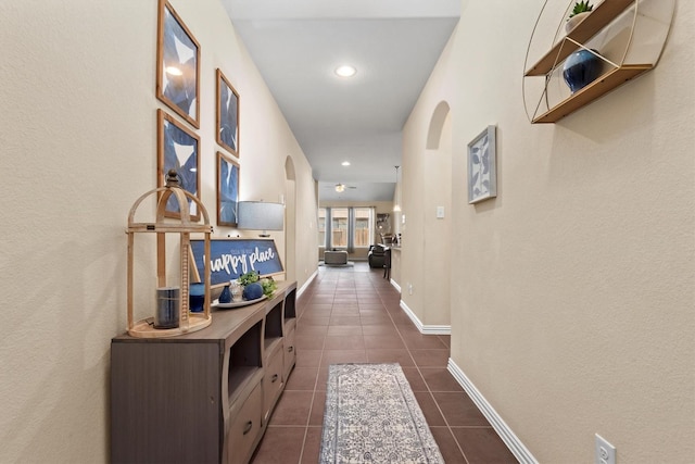 hall with dark tile patterned flooring, recessed lighting, arched walkways, and baseboards