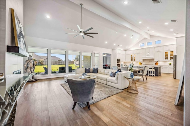 living room with a ceiling fan, visible vents, high vaulted ceiling, beam ceiling, and light wood-type flooring