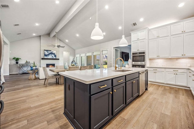 kitchen featuring a sink, a warm lit fireplace, white cabinetry, light countertops, and ceiling fan