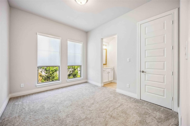 unfurnished bedroom featuring baseboards, light colored carpet, and ensuite bath