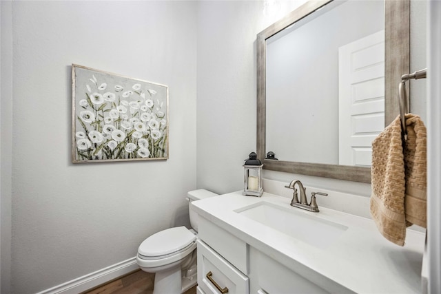 bathroom with toilet, vanity, baseboards, and wood finished floors