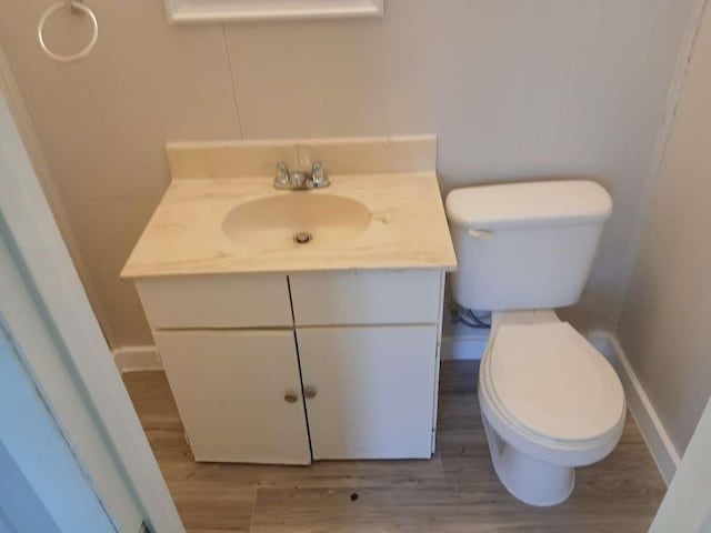 bathroom featuring baseboards, toilet, wood finished floors, and vanity