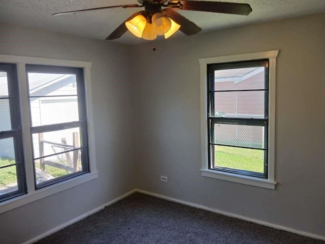 empty room featuring a healthy amount of sunlight, a textured ceiling, dark carpet, and baseboards