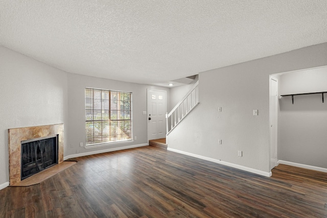 unfurnished living room featuring a textured ceiling, dark wood finished floors, stairway, a fireplace, and baseboards