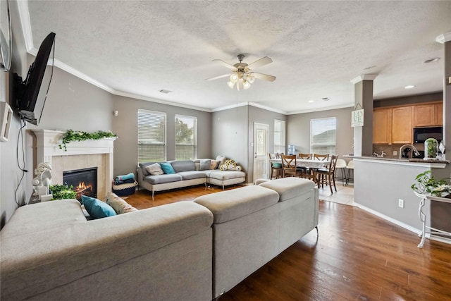 living area featuring crown molding, a tiled fireplace, hardwood / wood-style flooring, a textured ceiling, and a ceiling fan