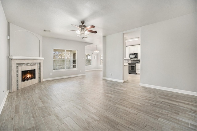 unfurnished living room featuring a tiled fireplace, ceiling fan with notable chandelier, a textured ceiling, light wood-style floors, and baseboards