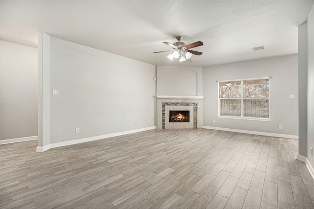 unfurnished living room featuring light wood-type flooring, visible vents, baseboards, ceiling fan, and a tile fireplace