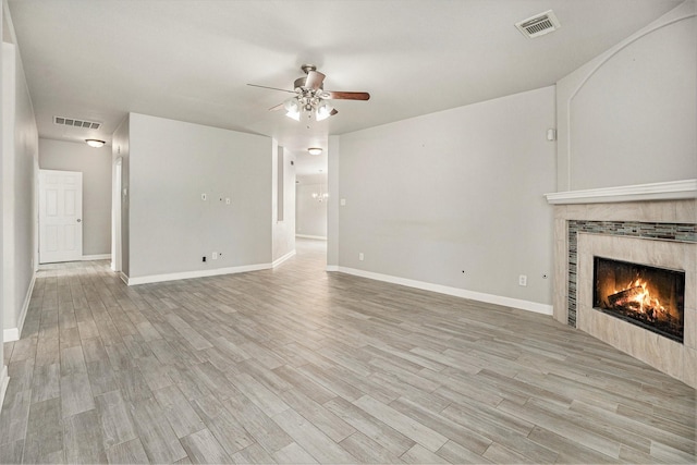 unfurnished living room with visible vents, a ceiling fan, a tiled fireplace, and light wood finished floors