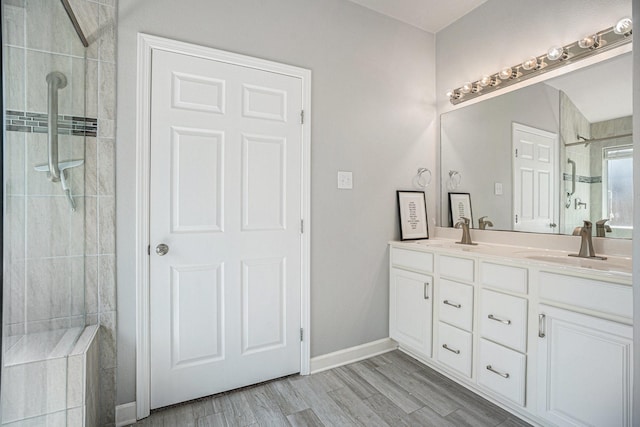 full bath with a sink, tiled shower, wood finished floors, and double vanity