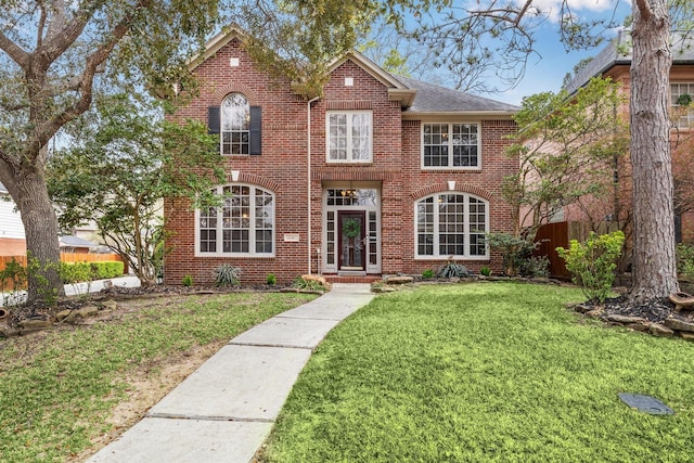 view of front facade with brick siding, a front yard, and fence