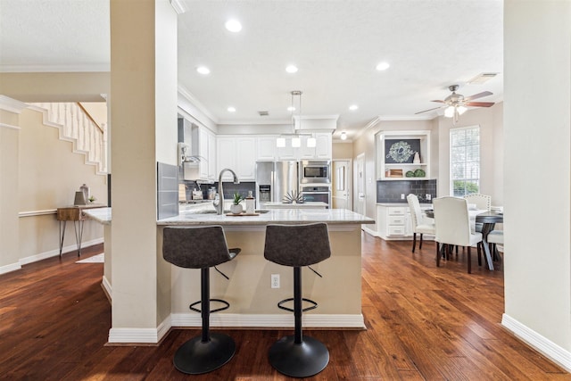 kitchen with dark wood-type flooring, a peninsula, a kitchen breakfast bar, white cabinets, and stainless steel appliances