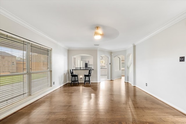 unfurnished living room featuring crown molding, wood finished floors, arched walkways, and baseboards