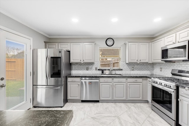 kitchen with tasteful backsplash, ornamental molding, dark stone countertops, appliances with stainless steel finishes, and a sink