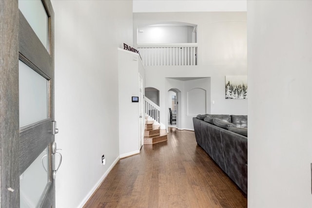 foyer with baseboards, stairs, hardwood / wood-style floors, a towering ceiling, and arched walkways